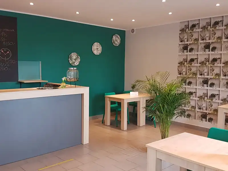 Sala z zieloną ścianą i białymi stolikami